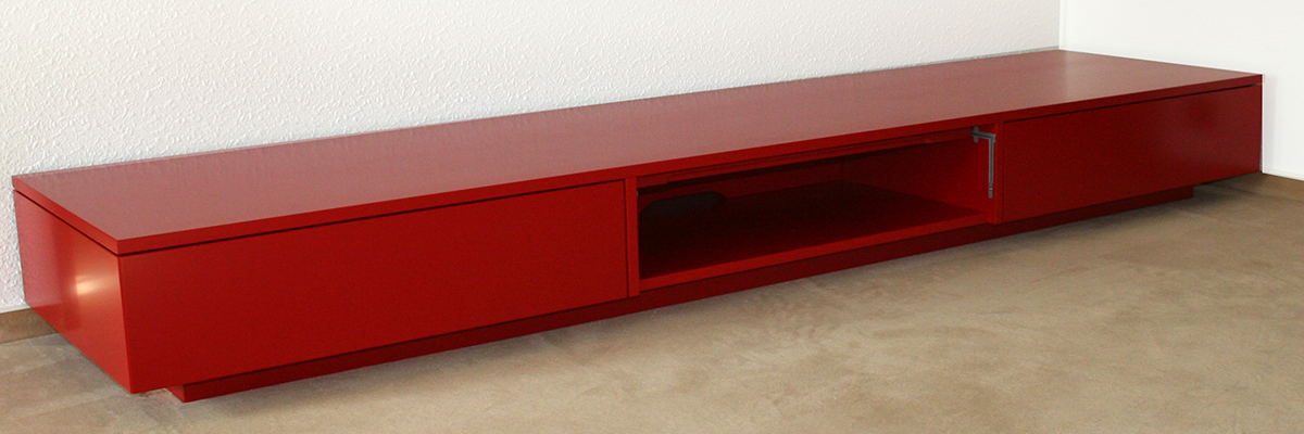 Der Schrank/ das Sideboard von der Tischlerei T&M-Möbeldesign. Der Schrank/ das Sideboard von der Tischlelrei T&M-Möbeldesign ist flach und komplett rot. In der Mitte befindet sich eine Öfnnung.