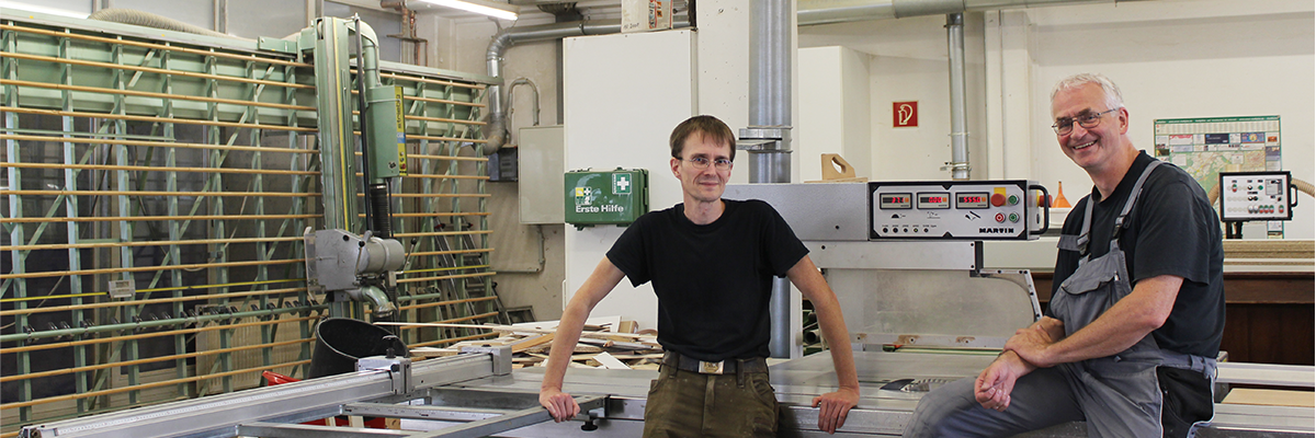 Tischlerei T&M-Möbeldesign Geschäftsführer. Auf der linken Seite steht Herr Markus Bovenkerk und auf der rechten Seite steht Herr Thomas Stille. Die beiden lehnen sich an eine Maschine an.