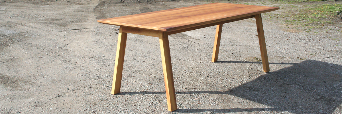 Der Holztisch von der  Tischlerei T&M-Möbeldesign ist in einem helleren brauen Ton und die Beine sind schräg gestellt.