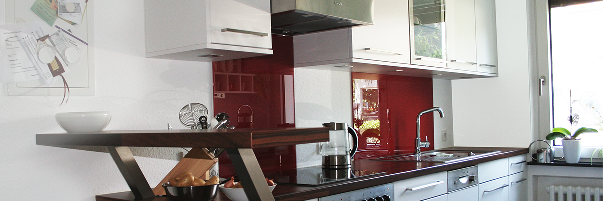 Tischlerei T&M-Möbeldesign Küche. Die Küche von der Tischlerei T&M-Möbeldesign ist in Weiß gehalten mit roten Glasplatten, welche als Highlight-Elemente integriert wurden.